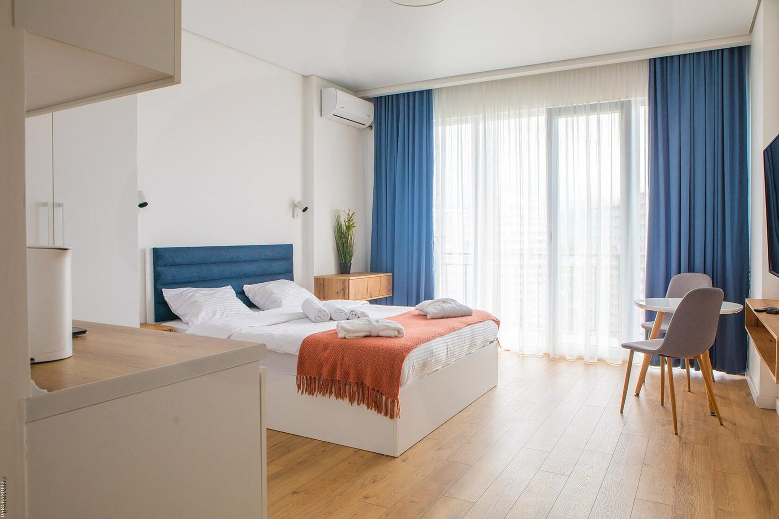 Furnished studio at NEXT Orange with blue curtains and an orange bed throw